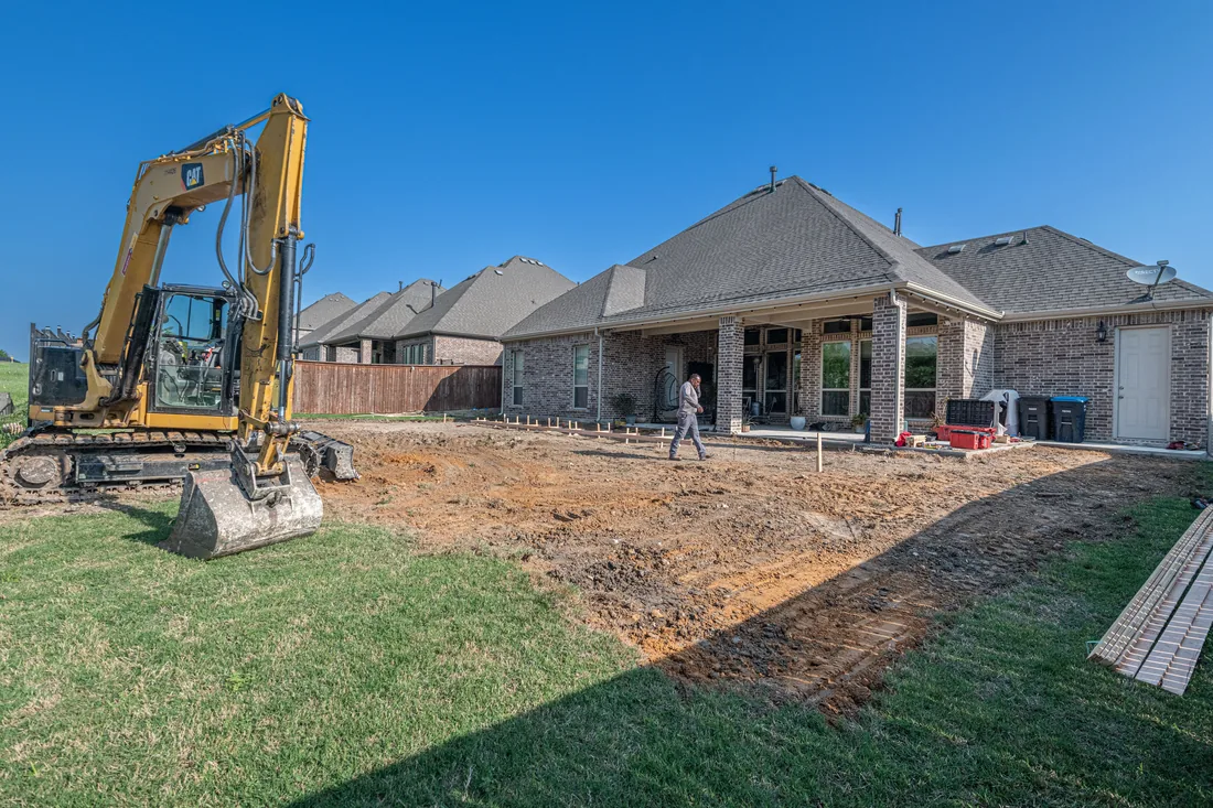 An excavator working a graded site beside a house during the ground stage